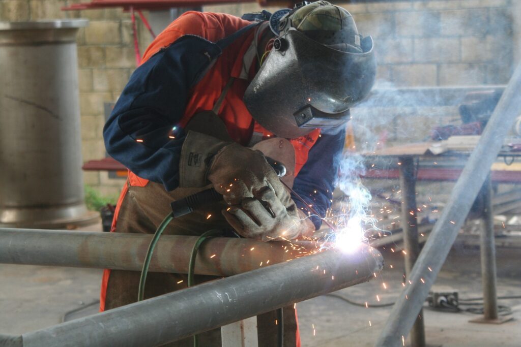 Welder occupied in welding a pipe while wearing a pearl snap shirt